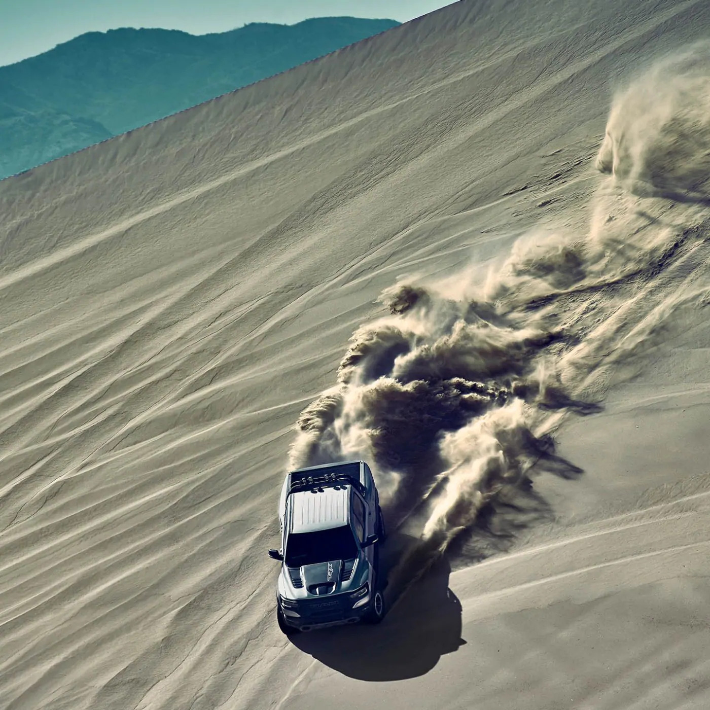 An aerial view of a 2021 Ram 1500 TRX being driven on a sand dune with a dust cloud marking its path.